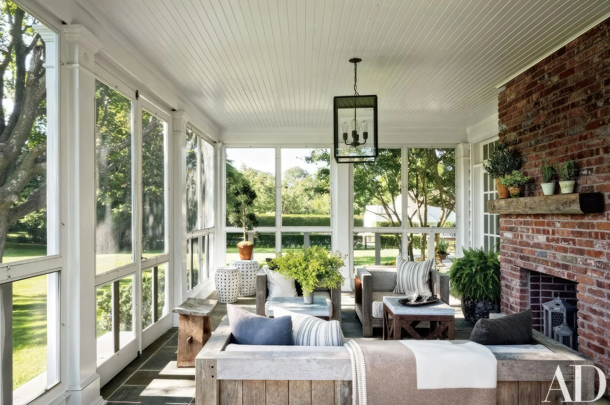 Charming screened-in porch featuring rustic wood furniture, a red brick fireplace, beadboard ceiling, and panoramic garden views.